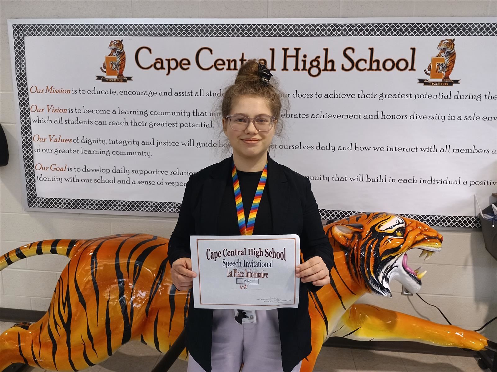  A girl with curly hair worn in an updo and glasses holds a certificate announcing 1st place.